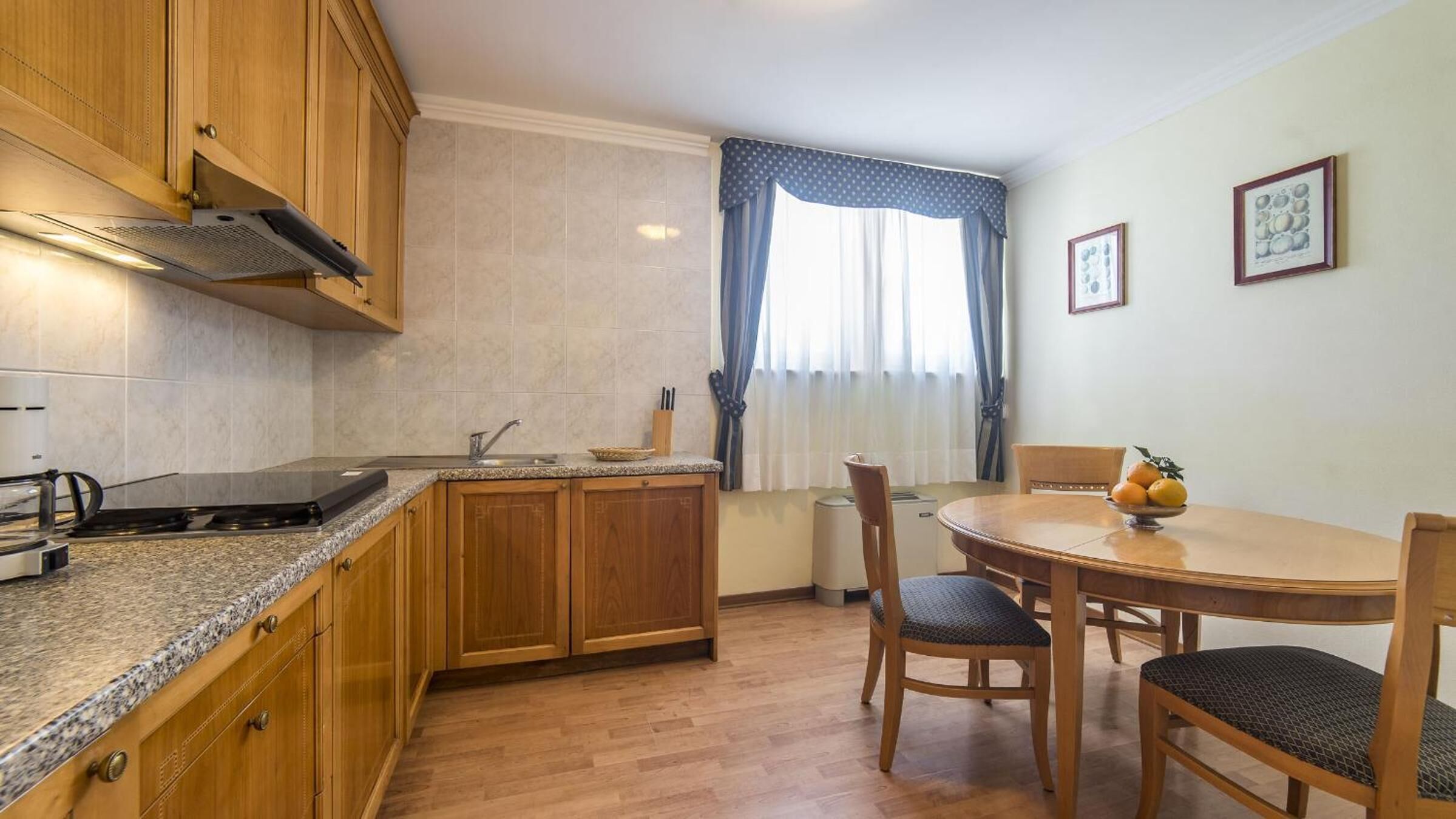 A compact kitchen with wooden cabinets, a granite countertop, a built-in stove, and a dining area with a round table and chairs.