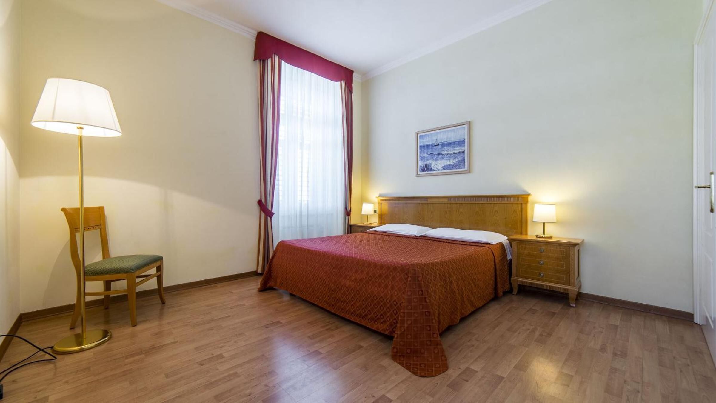 Ein Hotelzimmer mit einem hölzernen Bett, einem Sessel, einer Stehlampe und einem Bild an der Wand.