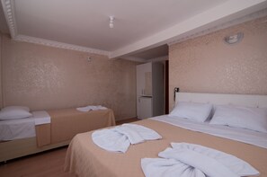 Ett hotellrum med två separata sängar, ett litet bord, ett kylskåp och en dörr som leder till ett annat rum.