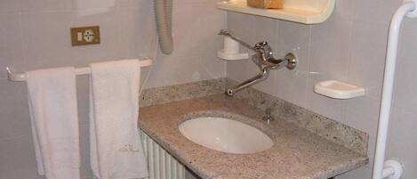 Une salle de bain avec un lavabo en granit, des carreaux blancs, un porte-serviettes, un miroir et une étagère contenant des articles de toilette.