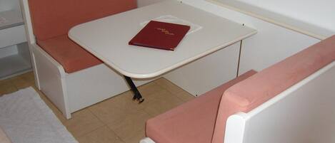A small room with a white table and two pink cushioned benches. A red book is placed on the table.