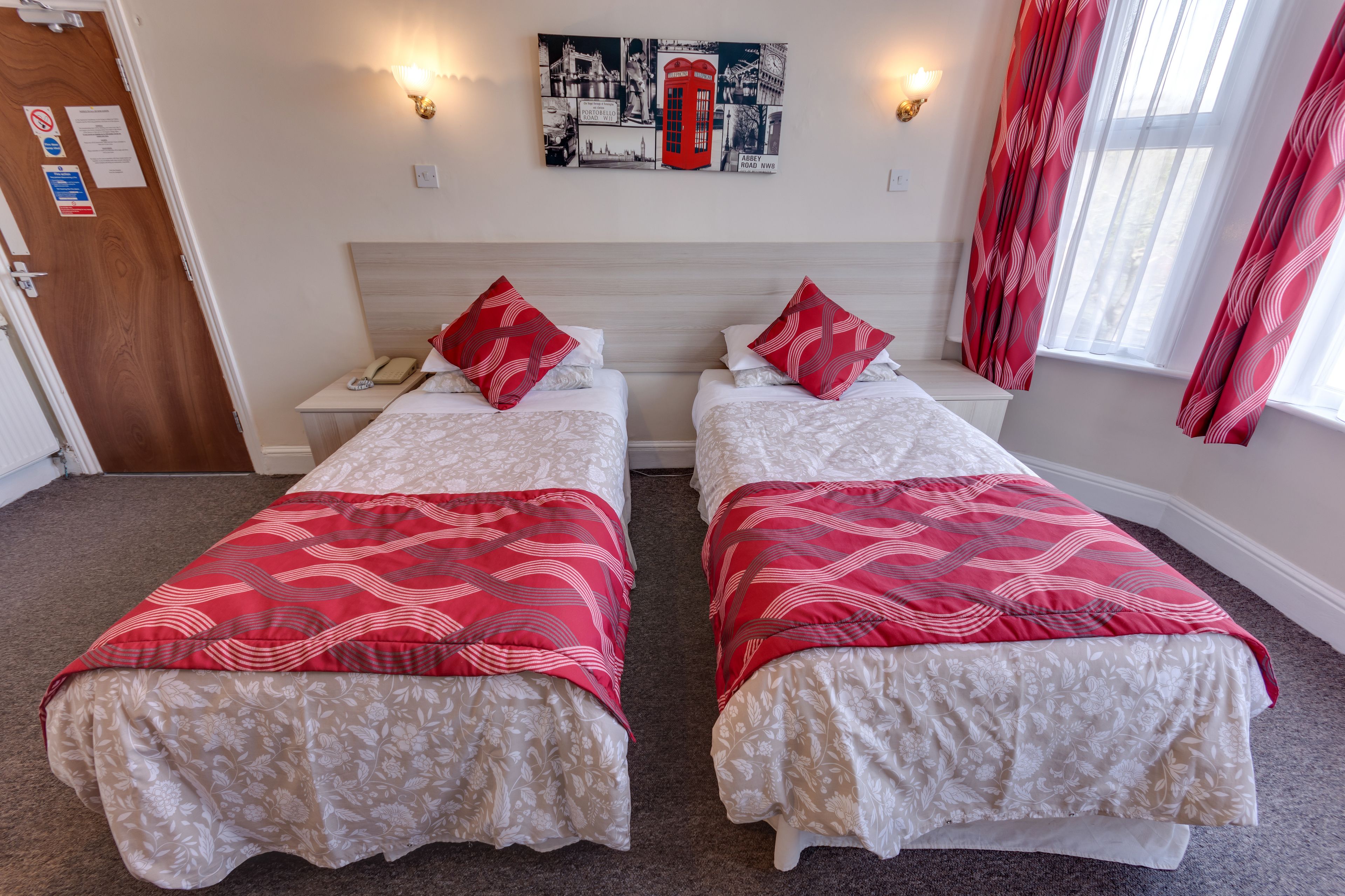 A hotel room with two beds, each with a red and white patterned bedspread, a wooden headboard, and a nightstand with a telephone.