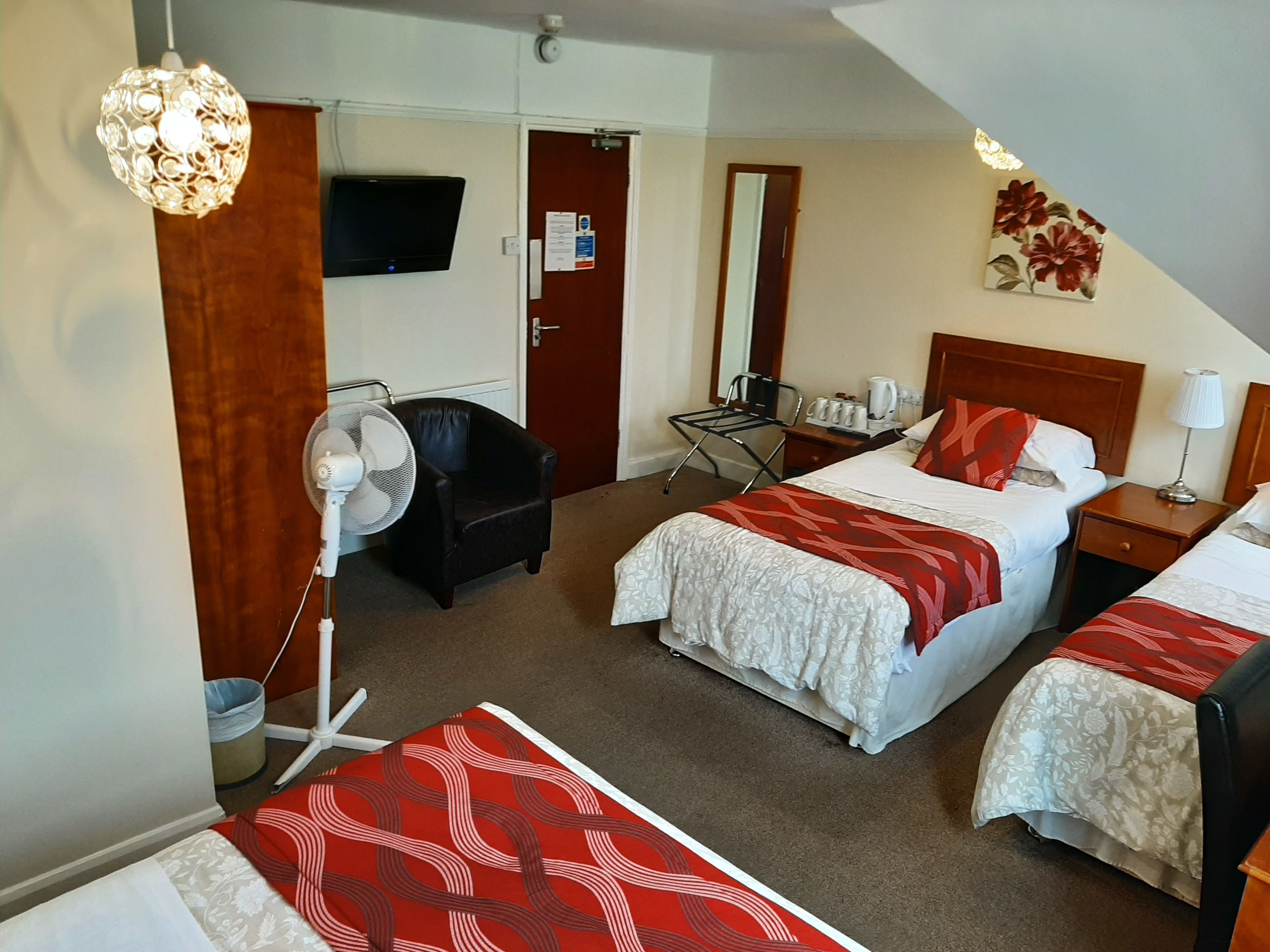 A hotel room with two beds, a desk, a chair, a fan, a TV, and a painting on the wall.