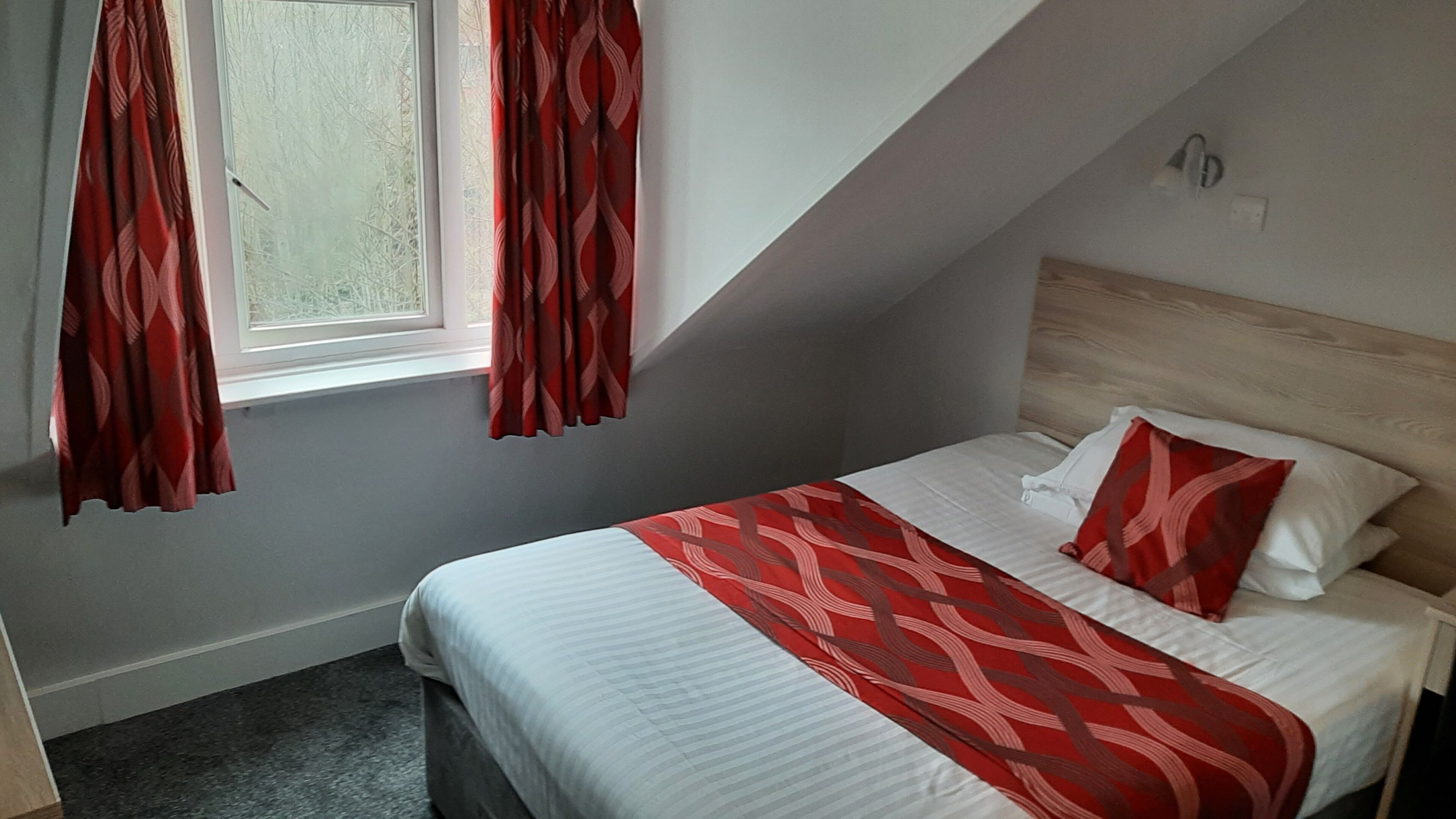 A bedroom with a bed, a window with curtains, a headboard, and a carpeted floor.