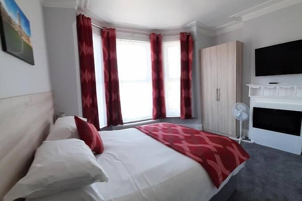 A bedroom with a bed, a wardrobe, a TV, and a window with curtains.