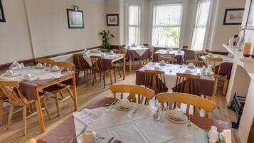Un espace repas avec plusieurs tables dressées, des chaises en bois et une grande fenêtre laissant entrer la lumière naturelle.