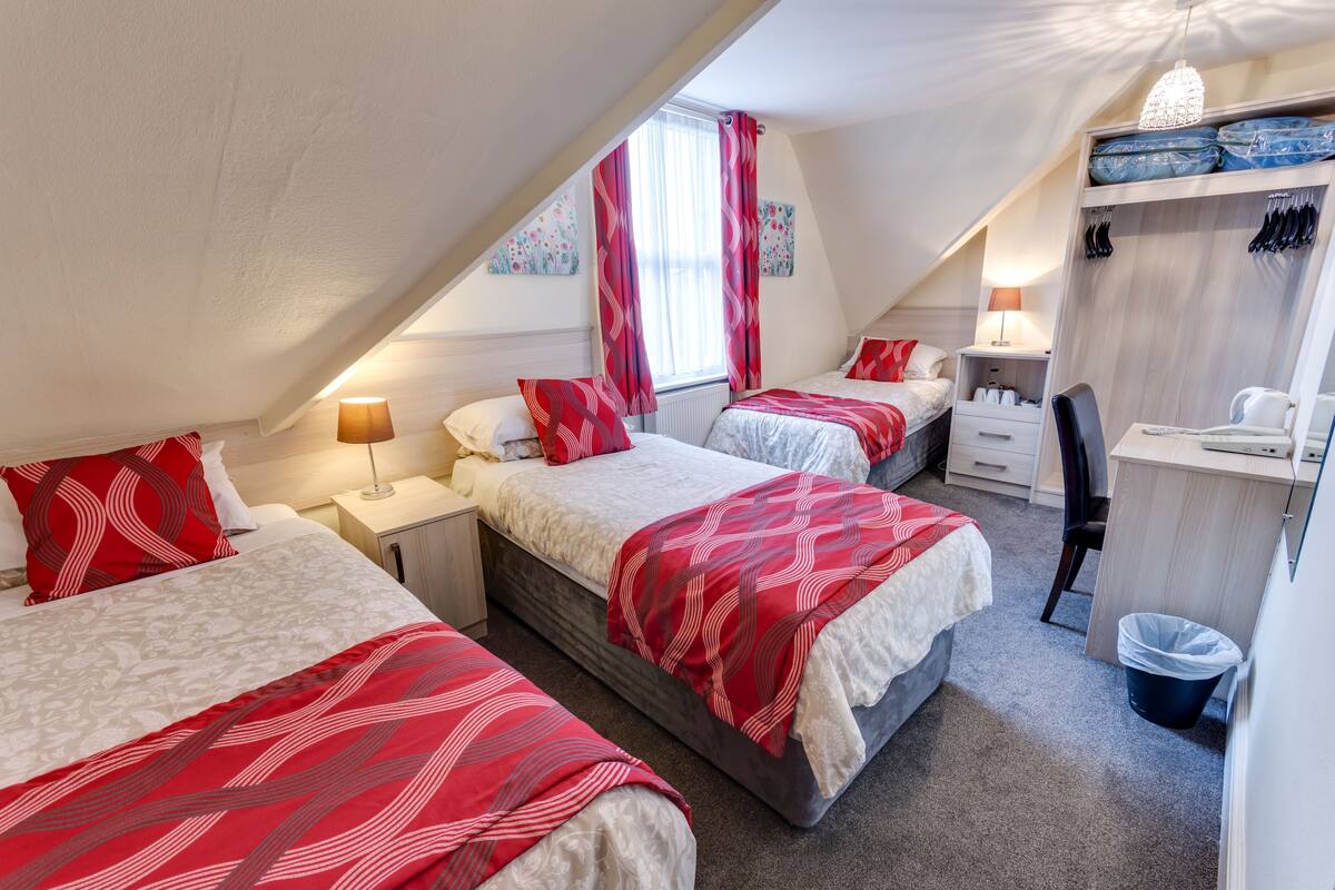 A cozy, well-lit attic bedroom with two beds, a desk, and a walk-in closet.