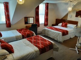 A hotel room with two beds, red and white bedding, a desk, a chair, a mirror, and a ceiling fan.