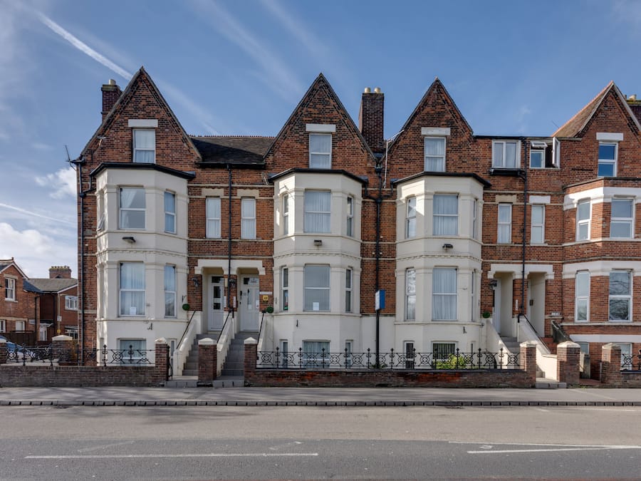 A row of red brick terraced houses with bay windows and white trim.