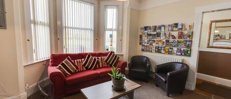 A living room with a red sofa, a wooden coffee table, a black leather armchair, and a wall with framed pictures.