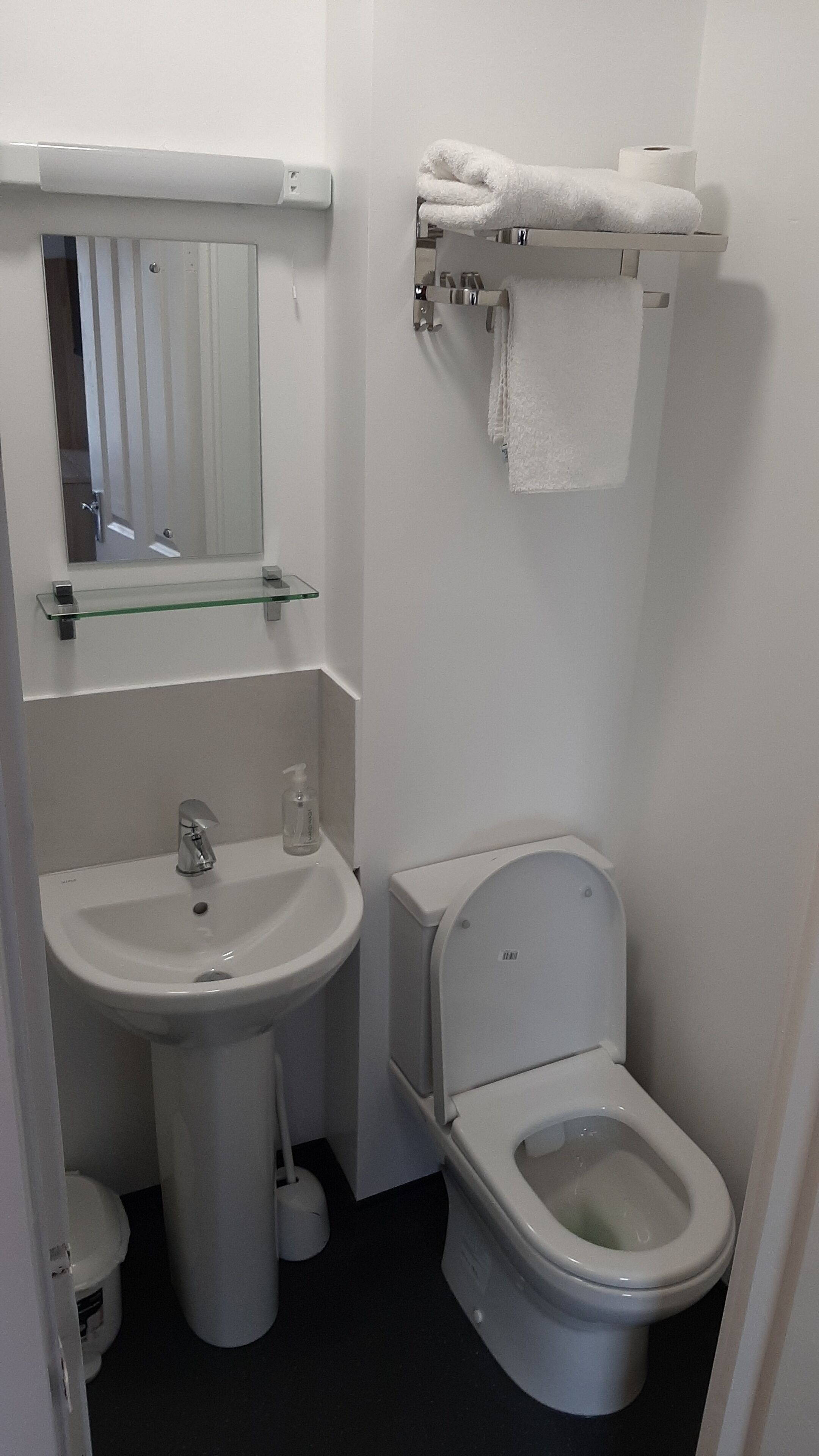 Un baño pequeño con lavamanos, espejo, inodoro y toallero.