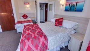 Ein Hotelzimmer mit zwei Betten, einem Kleiderschrank, einem Nachttisch und einem Bild an der Wand.