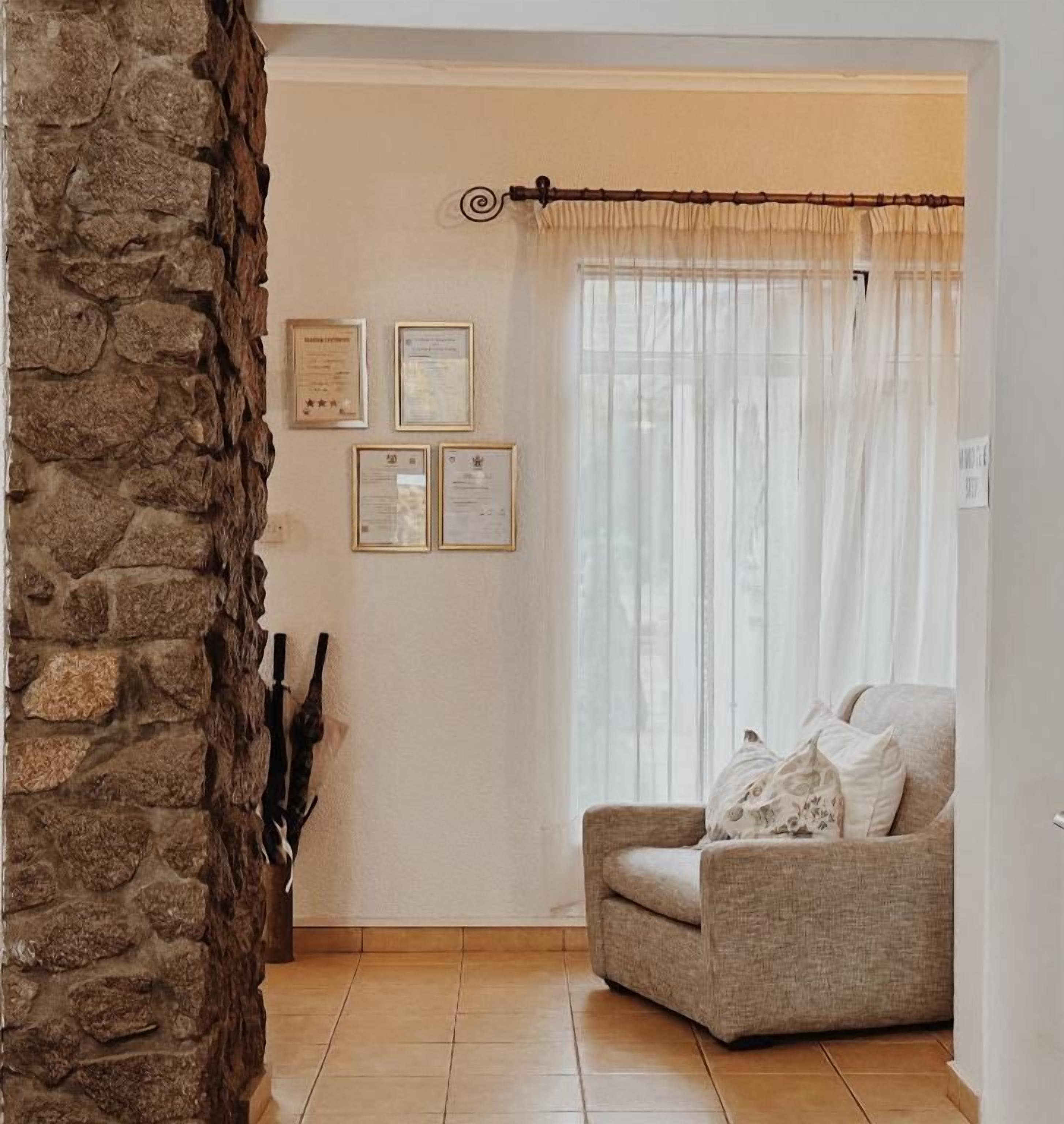 A corner room with a stone wall, a chair, and a window with sheer curtains.