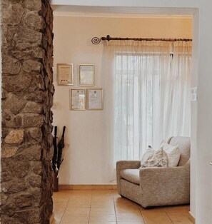 A corner room with a stone wall, a chair, and a window with sheer curtains. - Malcolm Lodge (Harare)