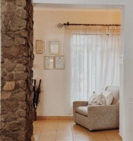 A corner room with a stone wall, a chair, and a window with sheer curtains.