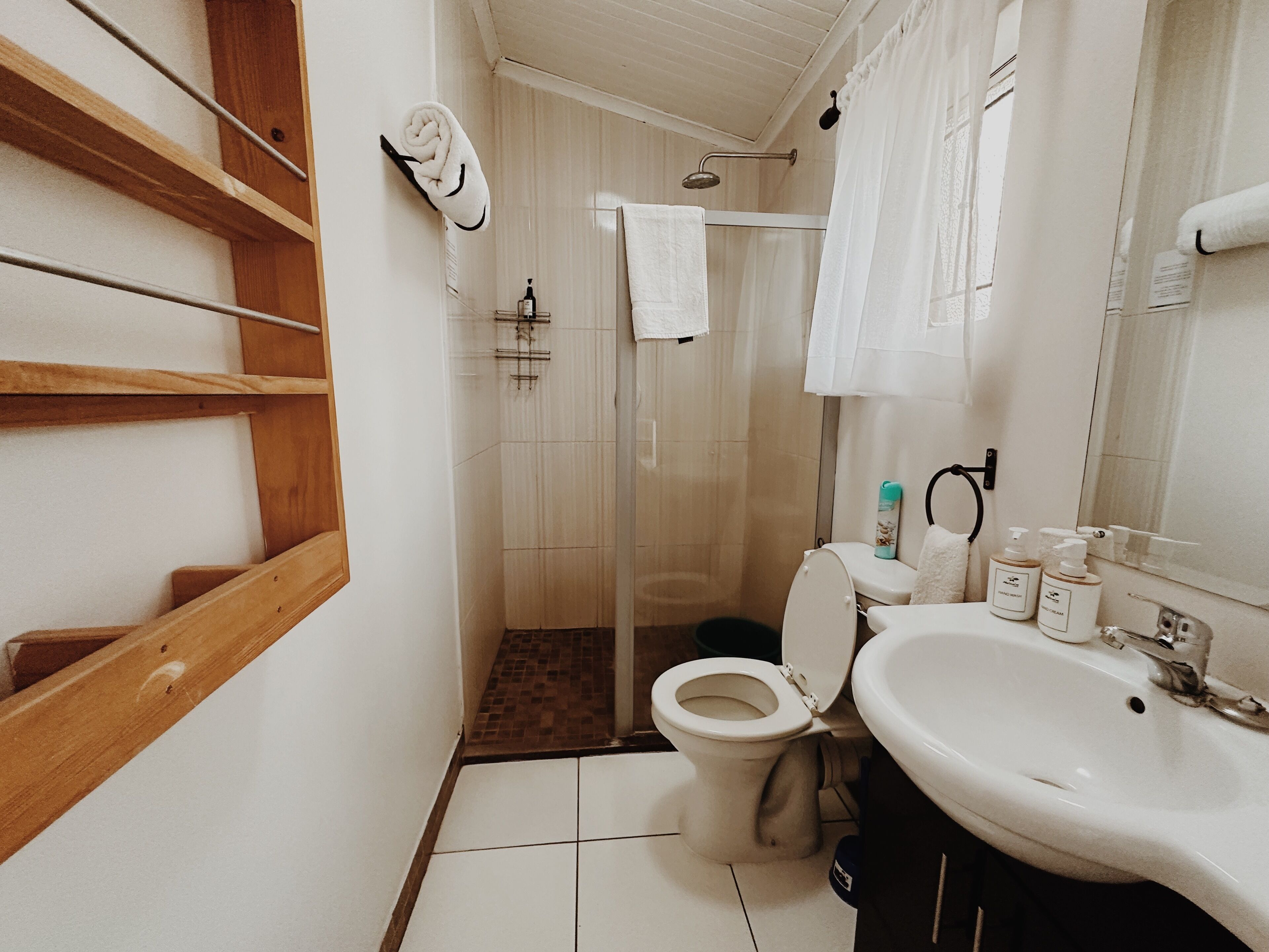 A bathroom with a toilet, shower, sink, and wooden shelves.