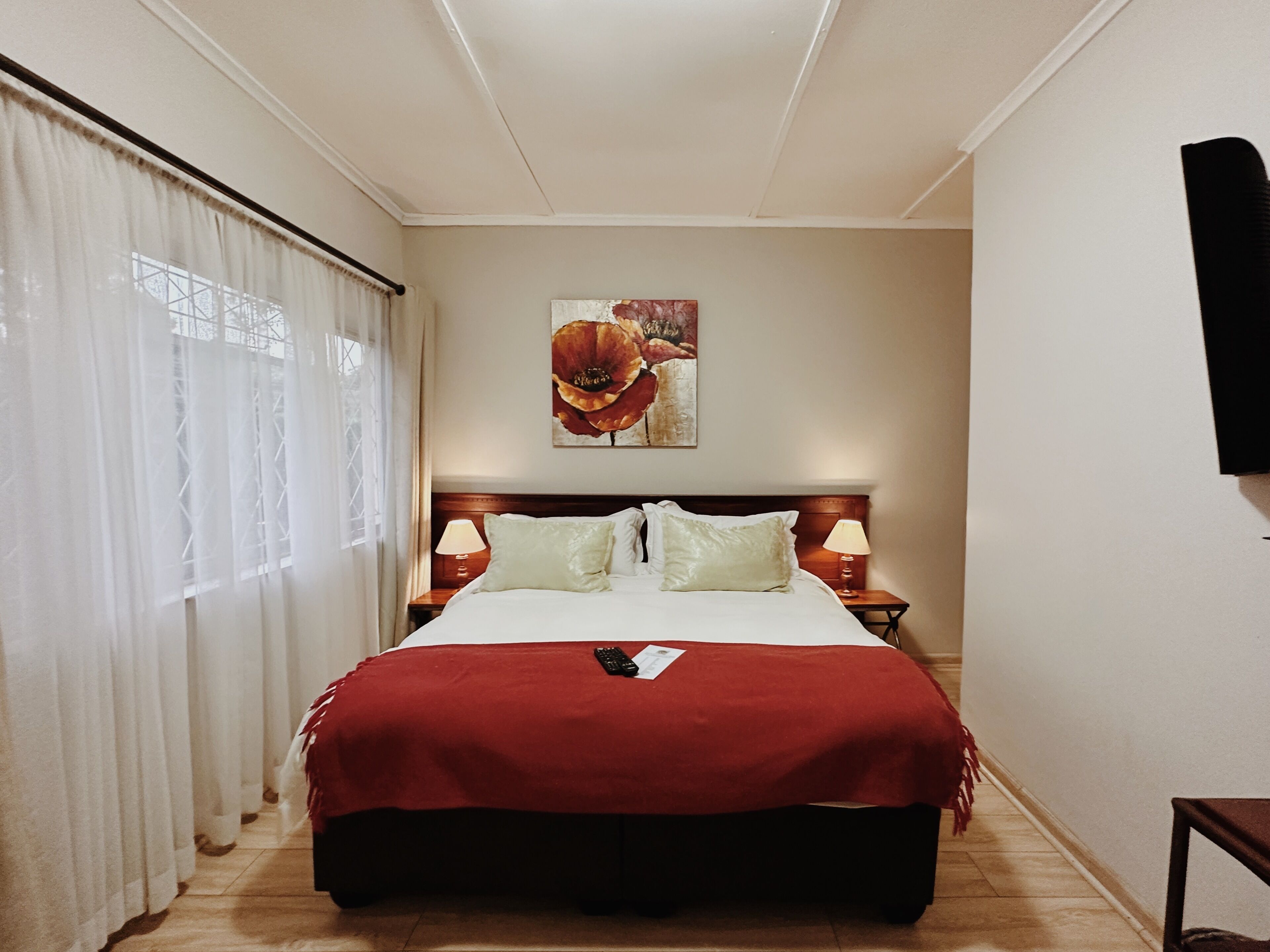 Una habitación de hotel con una cama grande, dos mesitas de noche con lámparas, un cuadro en la pared y un televisor montado en la pared.