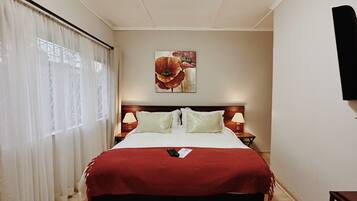 Una habitación de hotel con una cama grande, dos mesitas de noche con lámparas, un cuadro en la pared y un televisor montado en la pared.