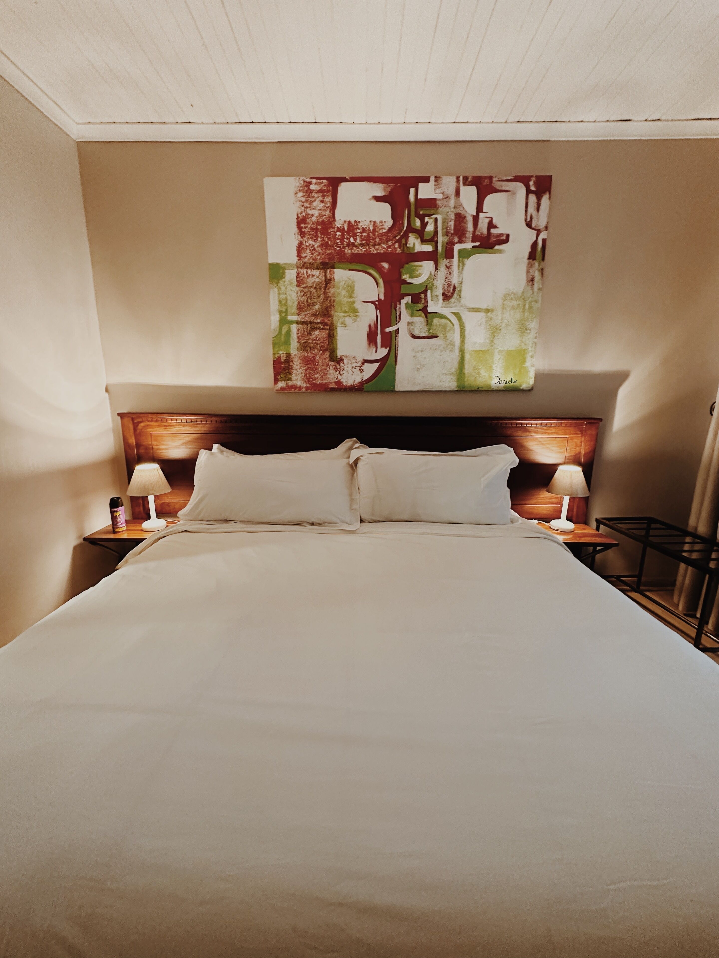 Een hotelkamer met een groot bed, twee bedlampen en een modern abstract schilderij aan de muur.