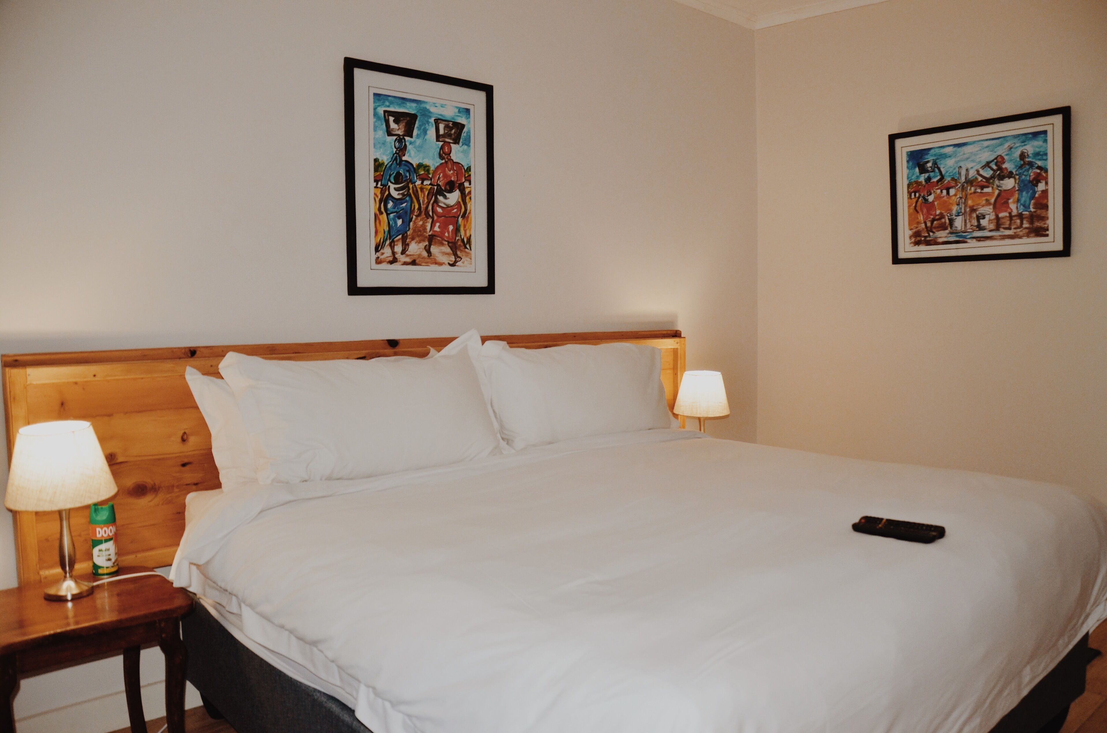 A neatly made bed with white linens, two bedside lamps, and a remote control on the bed.