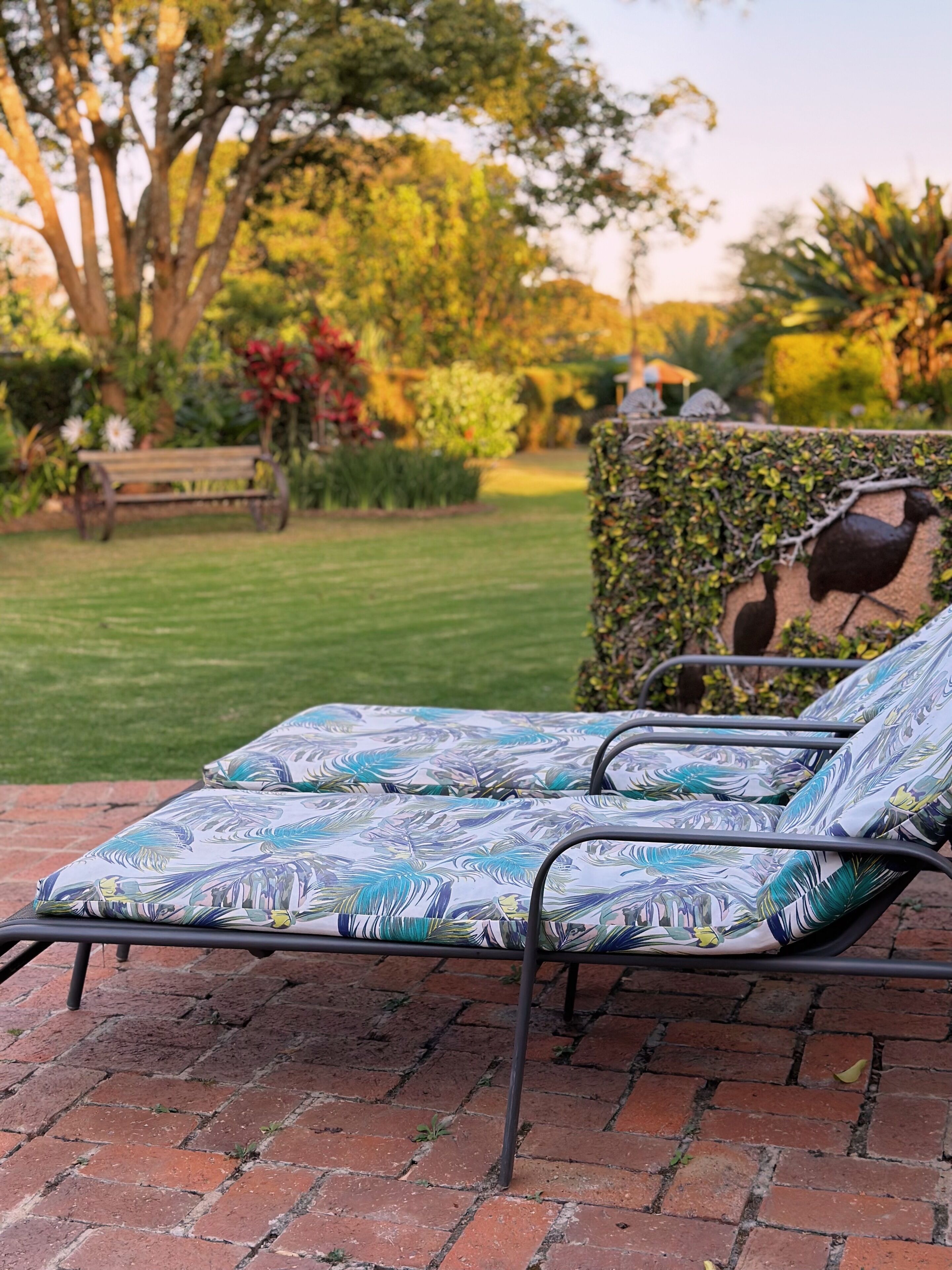 Un jardín con un banco, una silla de metal con cojín estampado y un muro de piedra con un diseño de pájaro.