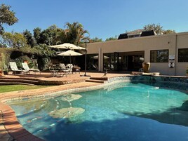 A swimming pool with a tiled deck, lounge chairs, and umbrellas.