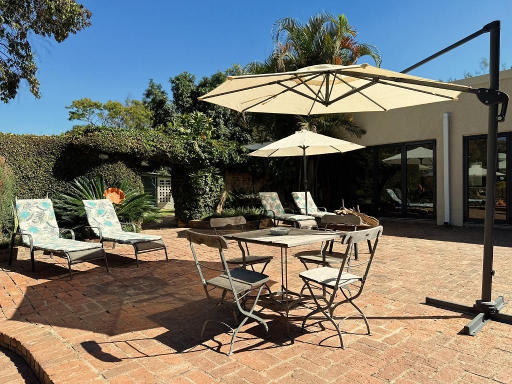 Um pátio externo com mesa, cadeiras, um grande guarda-sol e piso de tijolos.