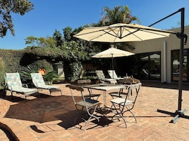 An outdoor patio with a table and chairs, a large umbrella, and a brick floor.