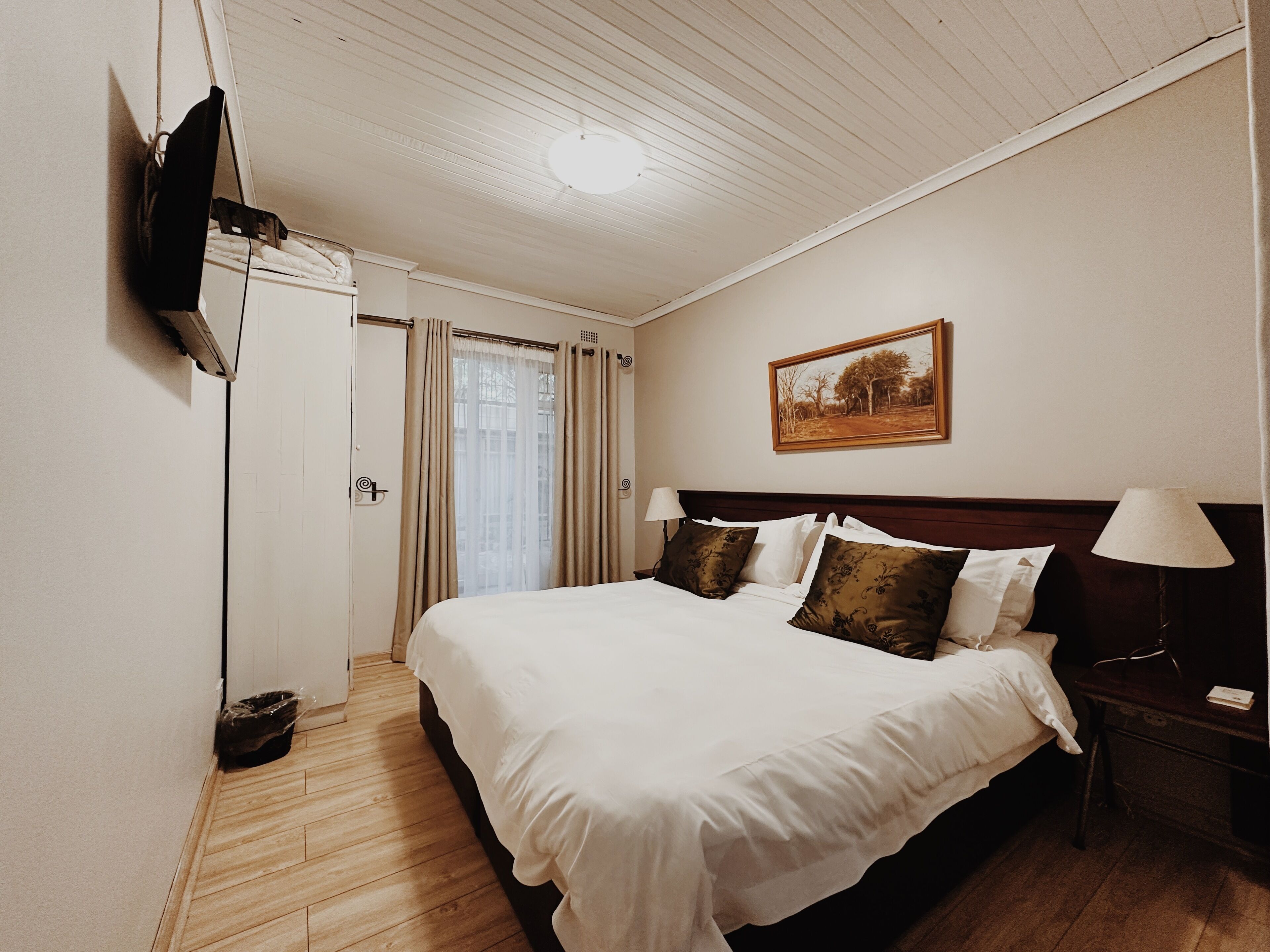 Una habitación de hotel con una cama, un cuadro en la pared, un televisor montado y suelo de madera.