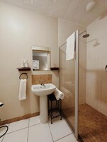 Un baño con lavamanos, espejo, toallero y ducha.