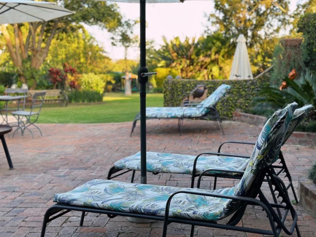 Un patio con dos sillones de descanso y una mesa, rodeado por un sendero de ladrillo y vegetación.