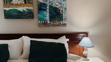 Un dormitorio con cama, almohadas, una mesita de noche, una lámpara y dos cuadros en la pared.