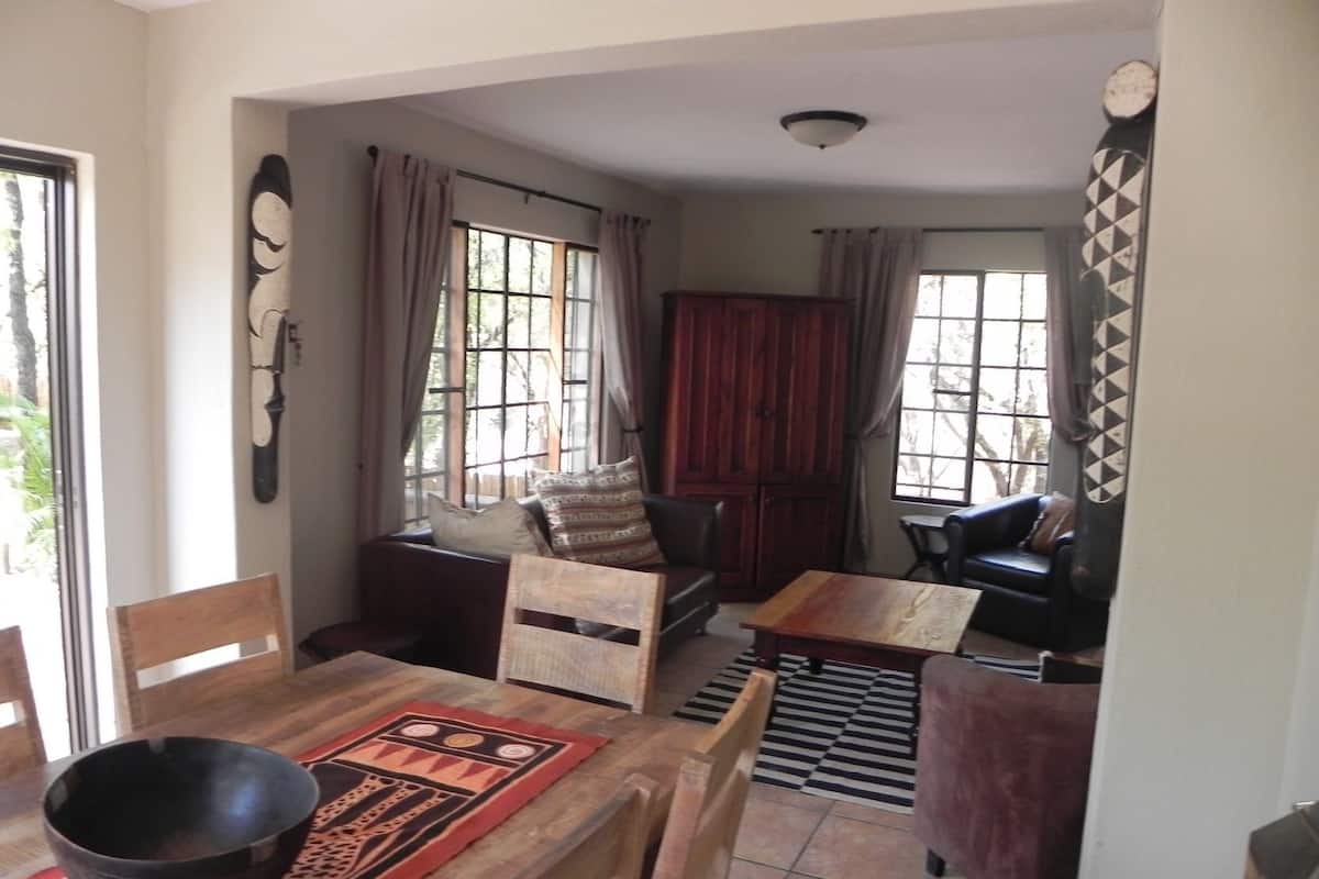 A dining area with a wooden table, chairs, and a large bowl. There is a sofa and a small table in the background.