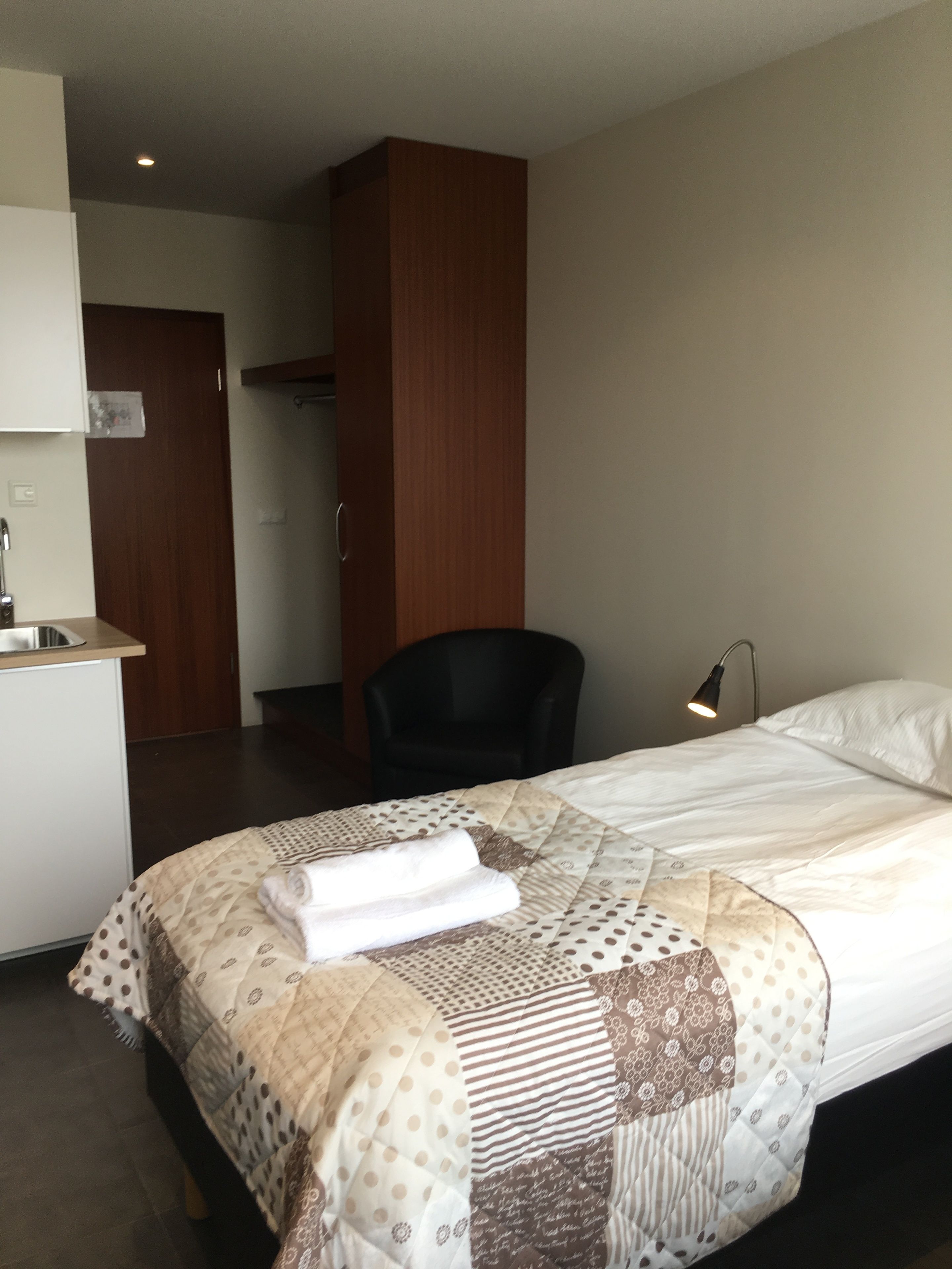 Une chambre d’hôtel avec un lit bien fait, un petit bureau doté d’un lavabo, une chaise et une lampe.