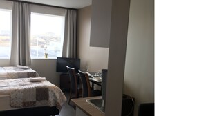 Een hotelkamer met twee bedden, een eettafel, stoelen, een televisie en een raam met gordijnen.