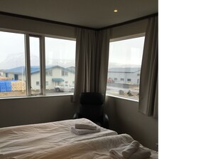 Ein Hotelzimmer mit Bett, einem Sessel und großen Fenstern mit Blick auf Gebäude und eine Straße.