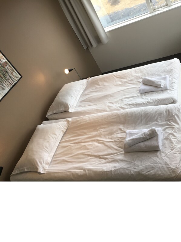 Ein Doppelbett mit weißer Bettwäsche und Kissen, eine Nachttischlampe und ein Fenster mit Vorhängen.