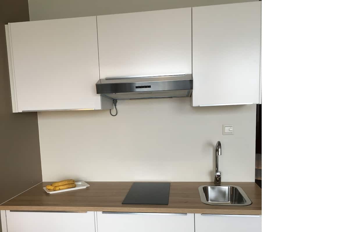 A kitchen with white cabinets, a stainless steel range hood, a sink, and a wooden countertop.