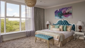 Une chambre avec une grande fenêtre, une tête de lit capitonnée, un banc et un tableau au mur.