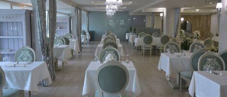 A formal dining room with multiple tables and chairs, elegant chandeliers, and decorative wall panels.
