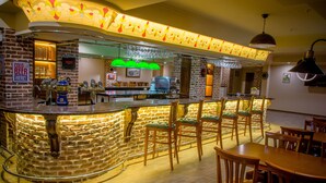 Un espace bar avec un comptoir en briques, des tabourets de bar et un coin salon avec des tables et des chaises en bois.
