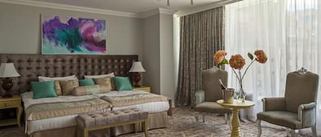 Una habitación de hotel con una cama grande, una zona de estar con una silla y una mesa, y un ventanal con cortinas.