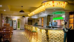 Un espace bar doté d’un comptoir en pierre, de chaises en bois et d’un luminaire vert suspendu.