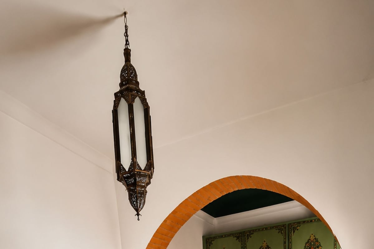 A bedroom with a bed, a desk, and a chair. There is a green door with decorative patterns.