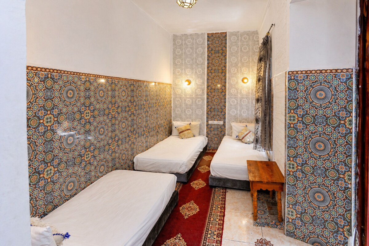 A room with two single beds, a small wooden table, and patterned walls.