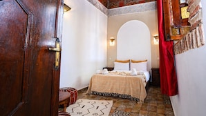 A room with a bed, a wooden door, a patterned rug, and a tiled floor. - Riad O-ly (Marrakech)