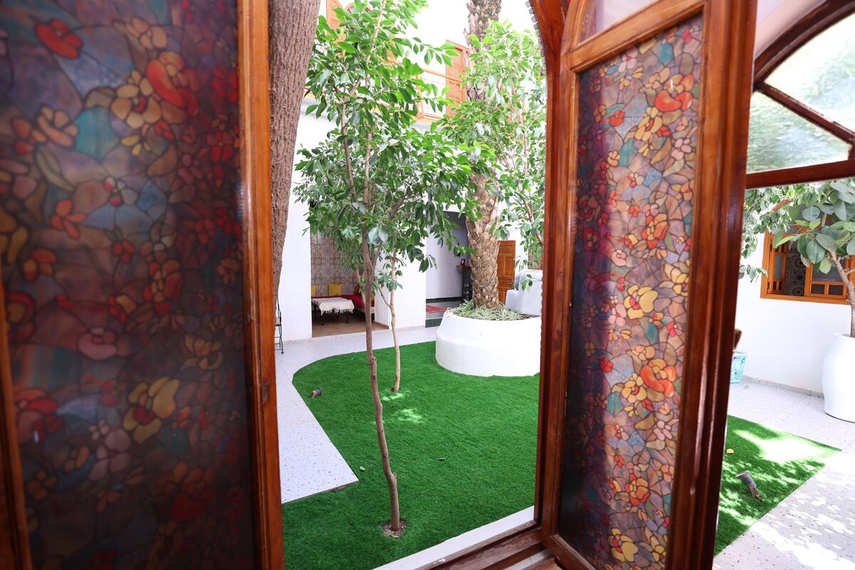 A view through a doorway with a stained glass window, a small tree, and a white wall.