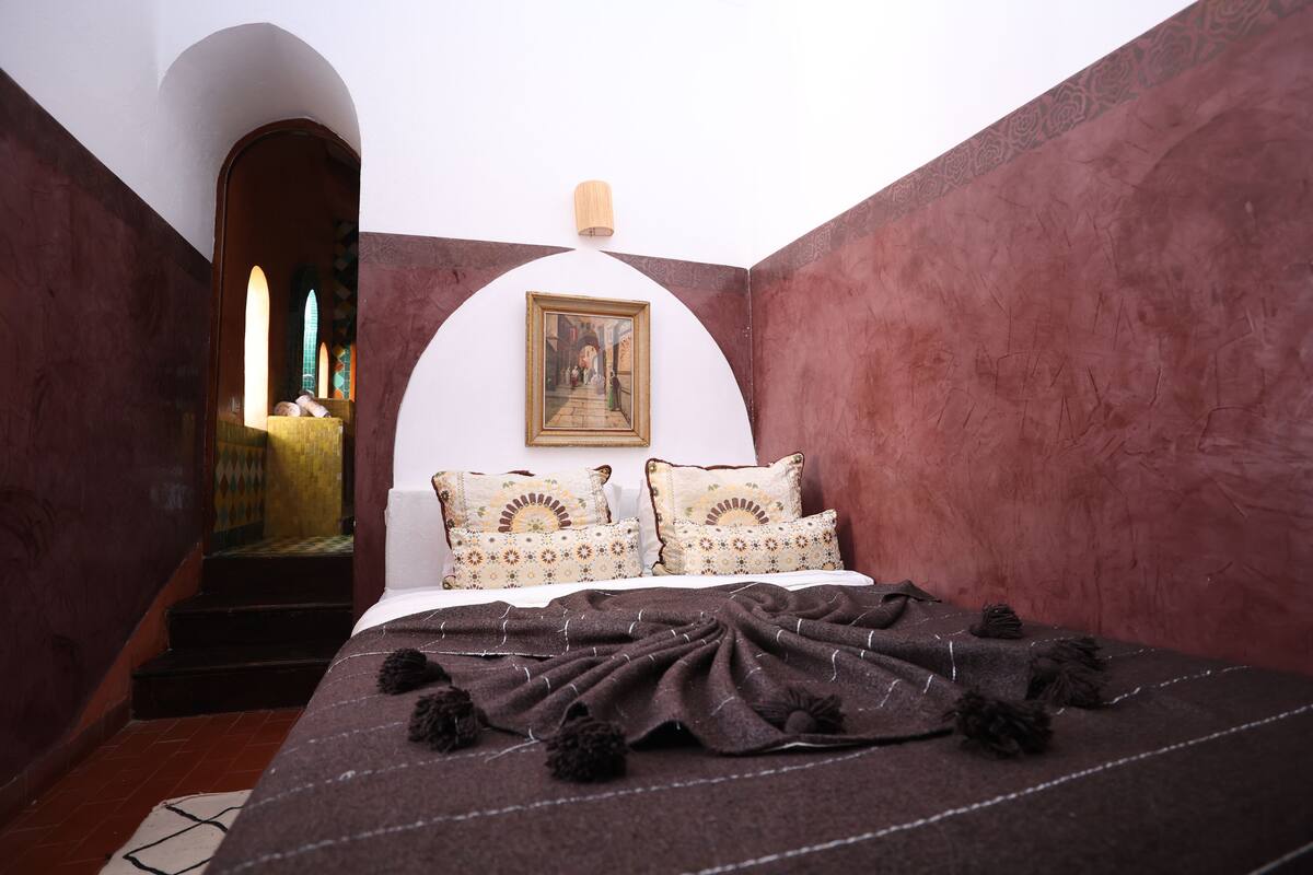 A bedroom with a bed, pillows, a blanket, and a painting on the wall.