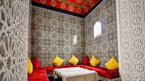 A room with patterned walls, a table with a white cloth, and red and yellow pillows. - Riad O-ly (Marrakech)