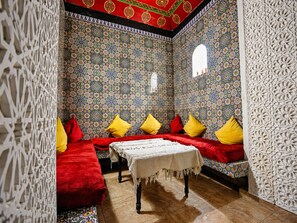 A room with patterned walls, a table with a white cloth, and red and yellow pillows. - Riad O-ly (Marrakech)